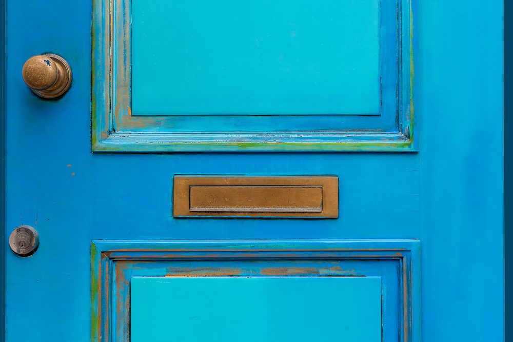 A brass letter slot in the centre of a weathered bright blue front door, with a brass knob and lock alongside