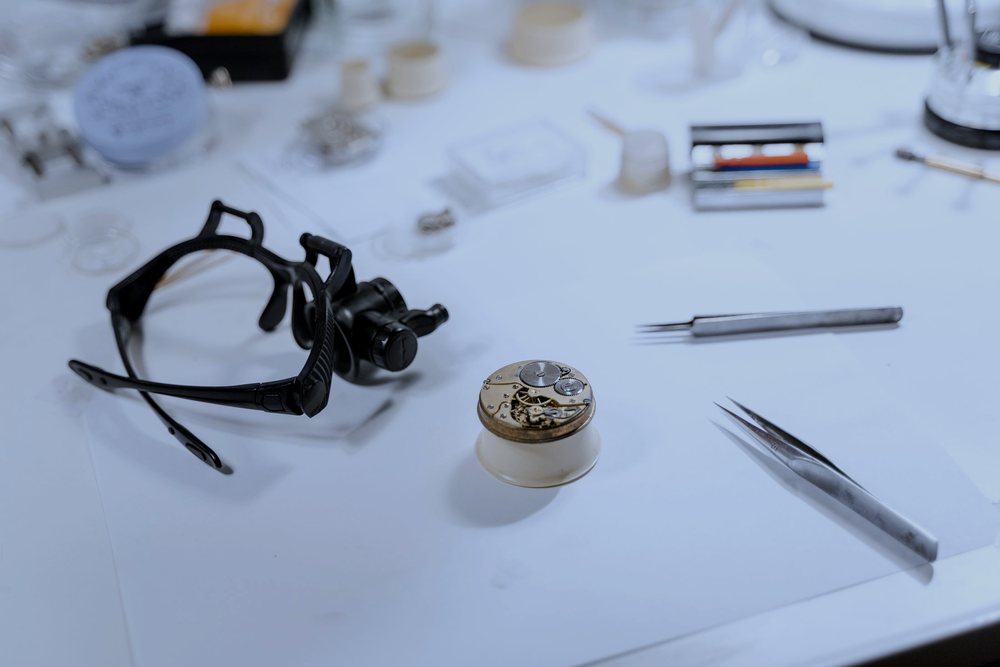A watchmaker's bench with a loupe, tweezers and a watch movement part way through a repair